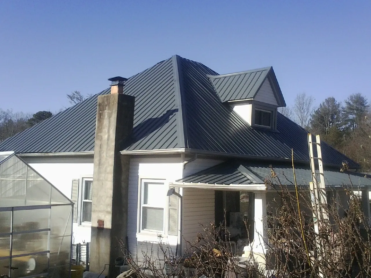 Dark blue standing seam metal roof on a white farmhouse with dormer — Slate & Tile Roof Repair by Roofing Brothers in Fountain