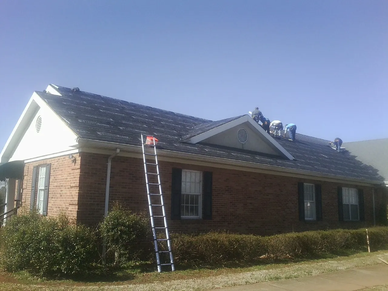 Crew tearing shingles off a brick ranch roof with a ladder set — Metal Roof Repair work by our crew in Fountain